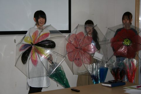 絵を描いたビニール傘を開いて見せる学生たち